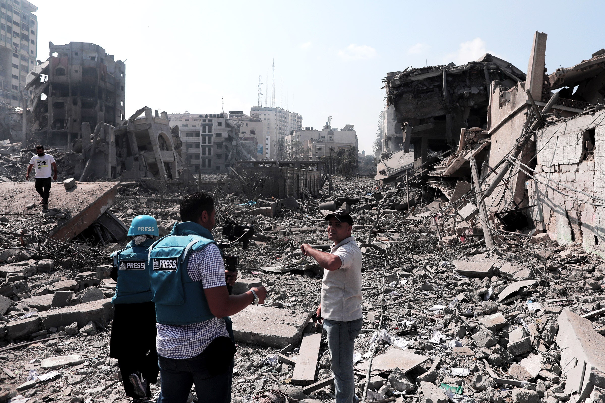 People wearing press vests filming while walking through rubble and debris from destroyed buildings